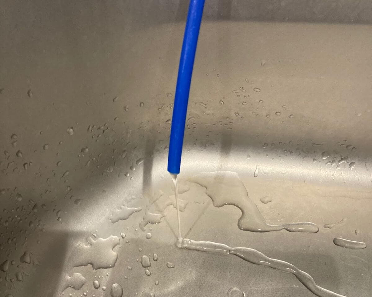 青い管の先からキッチンシンクに落ちる水滴